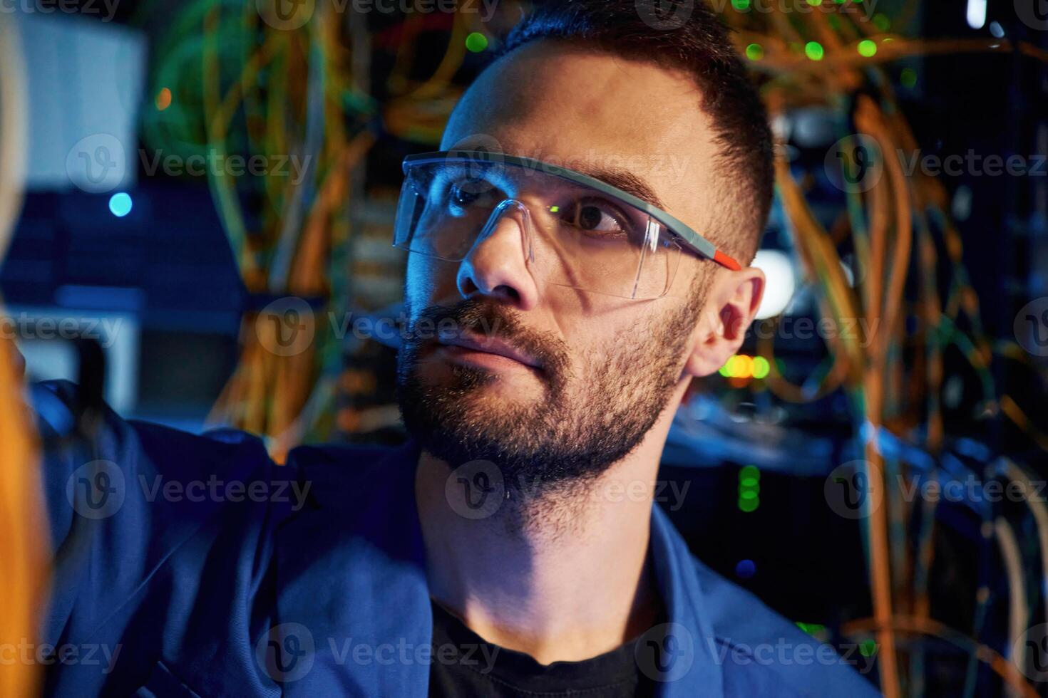 Handsome, young man is working with internet equipment and wires in server room photo