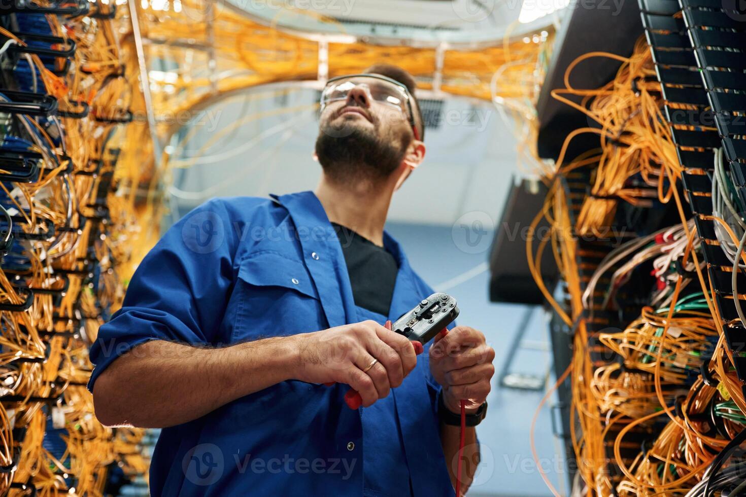 Busy by, cutting, the wire. Young man is working with internet equipment in server room photo