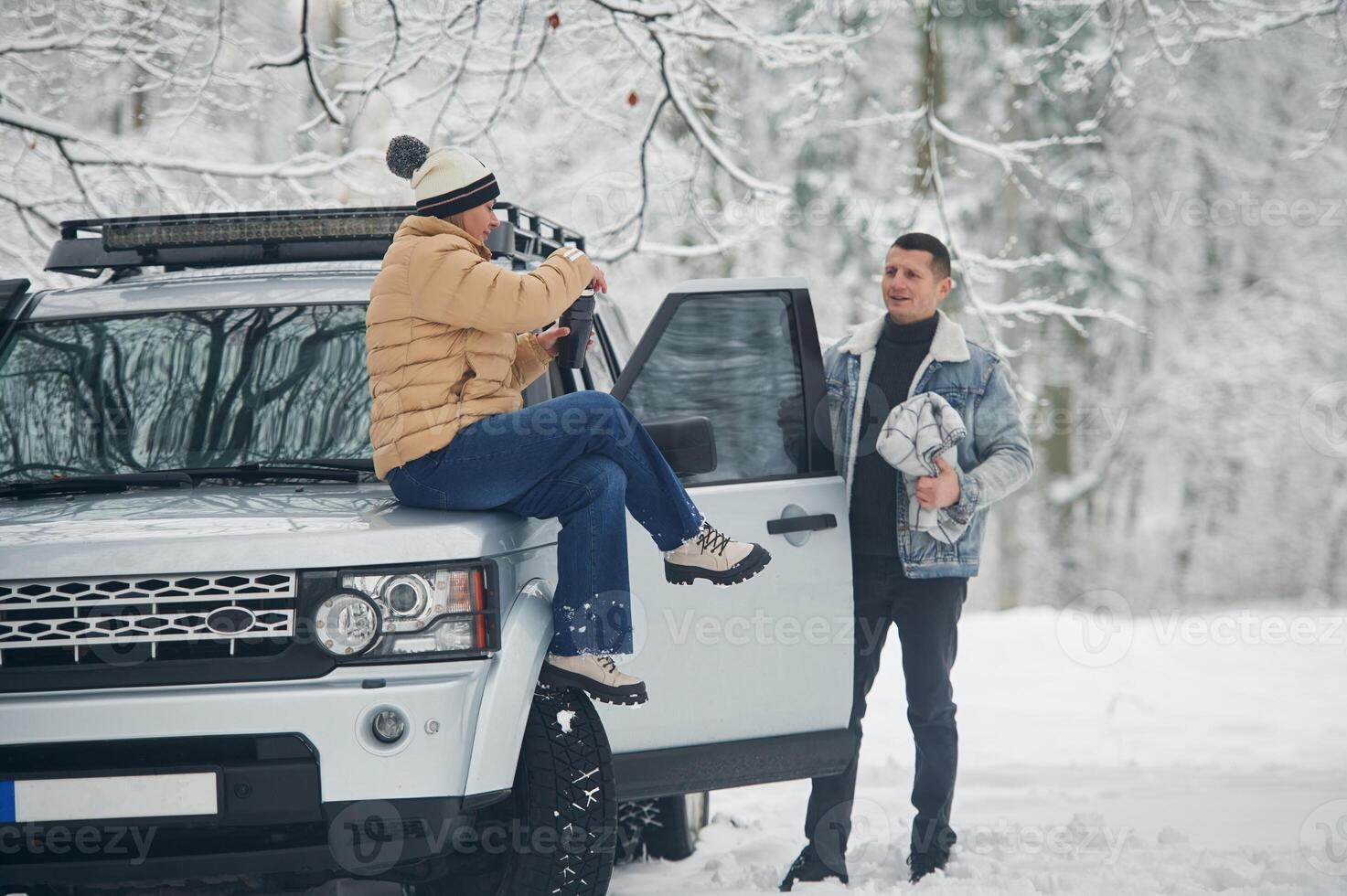 Woman ,is sitting on the car. Beautiful couple standing in the winter forest photo