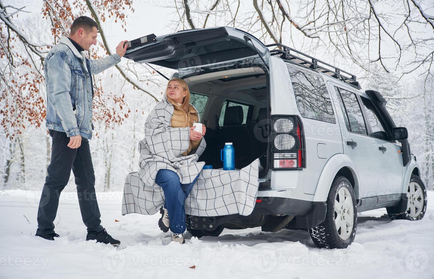 Woman ,,is sitting in the trunk. Beautiful couple standing near the car in the winter forest photo