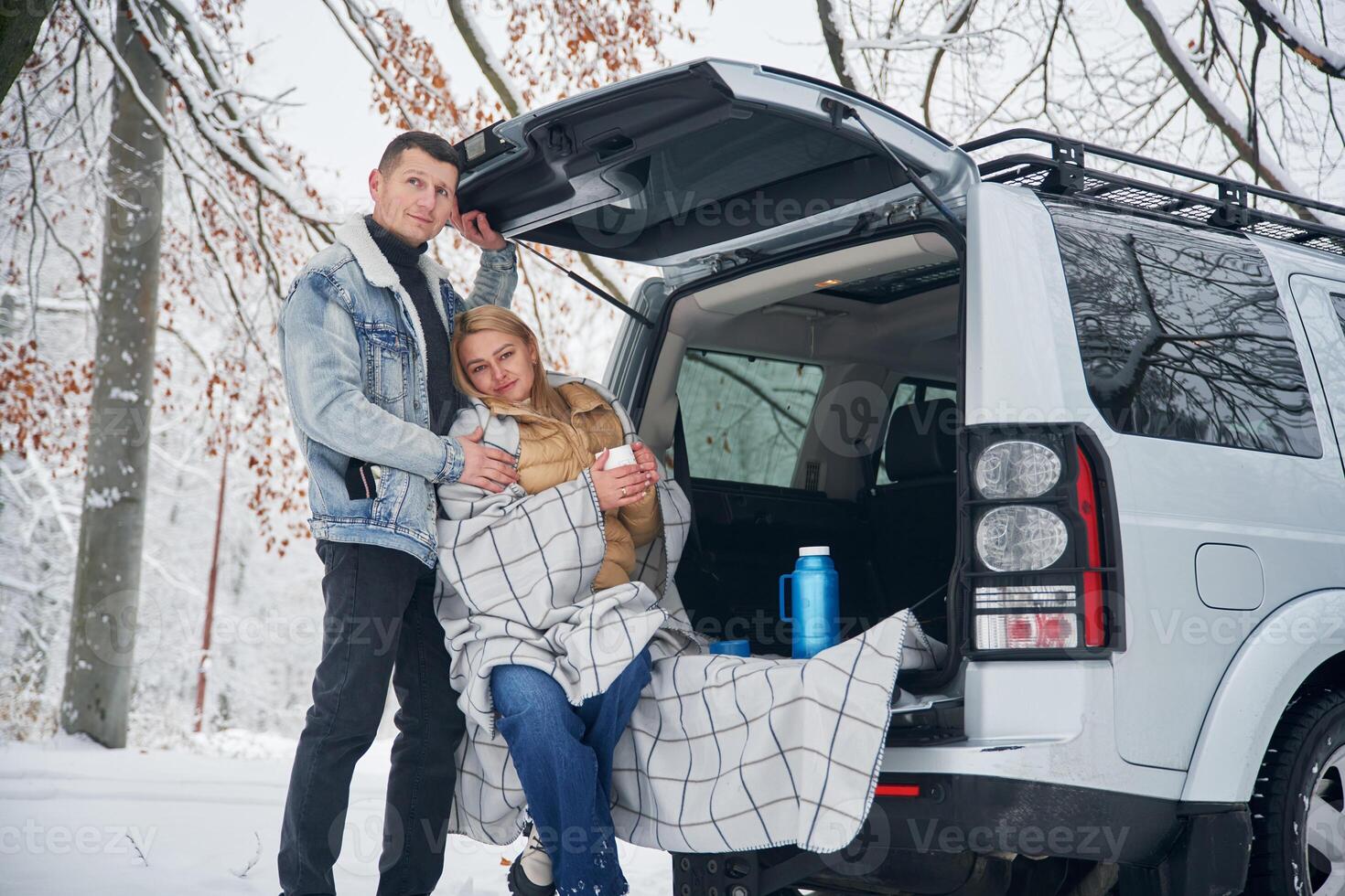 Woman is sitting ,in the trunk. Beautiful couple standing near the car in the winter forest photo