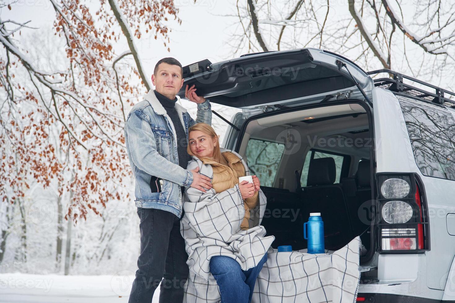 Woman, is sitting in the trunk. Beautiful couple standing near the car in the winter forest photo