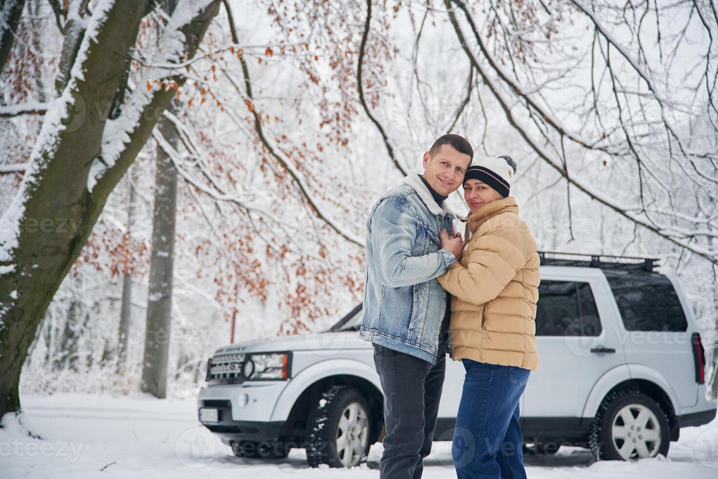 Standing and, posing. Beautiful couple are near the car in the winter forest photo