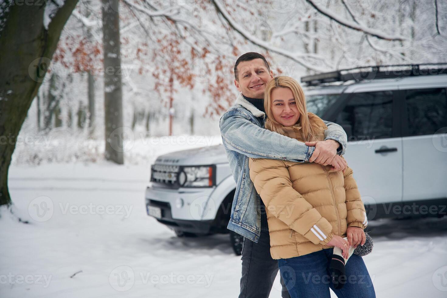Standing and,, posing. Beautiful couple are near the car in the winter forest photo