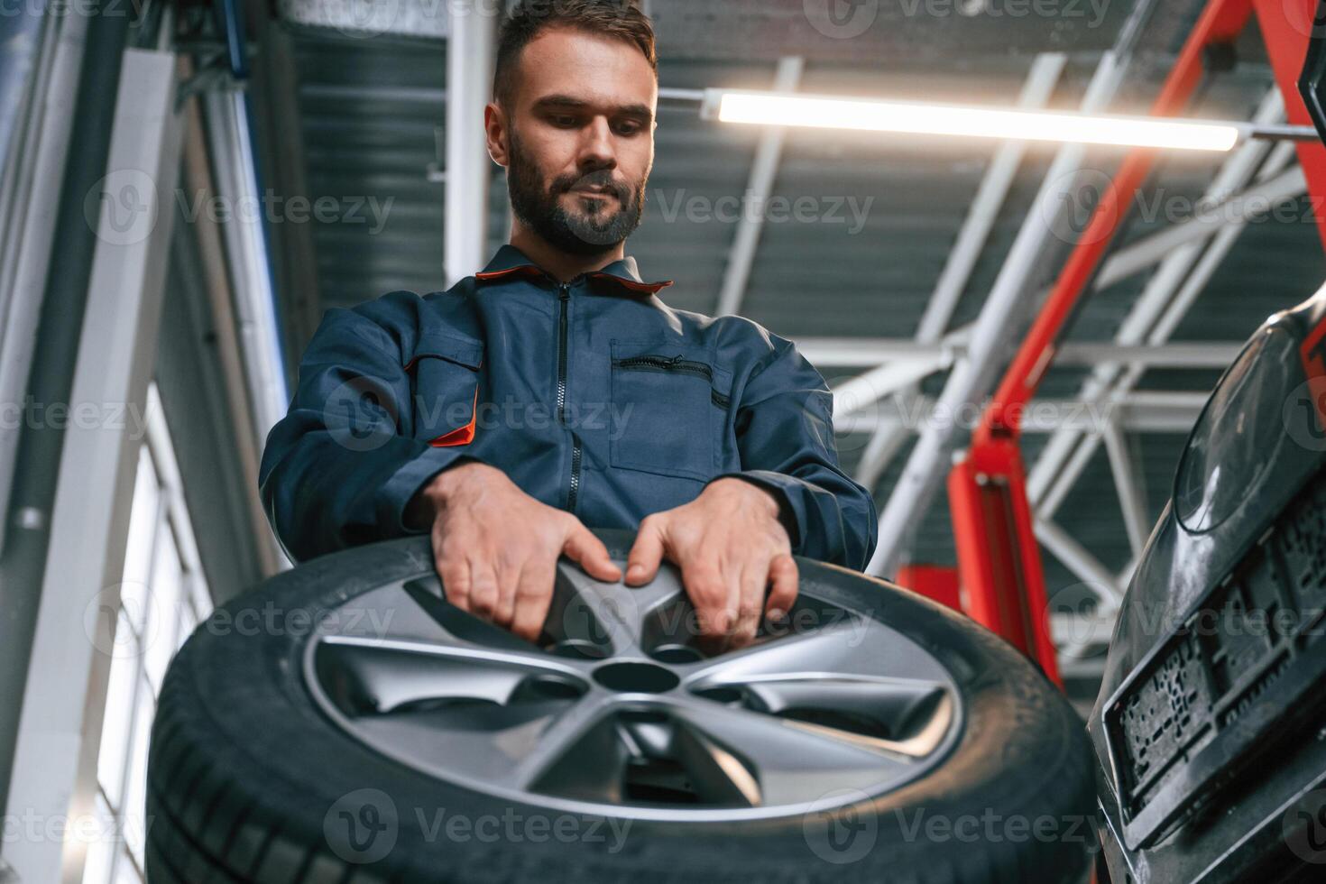 With ,,brand new tire. Car repairman is in the garage with automobile photo