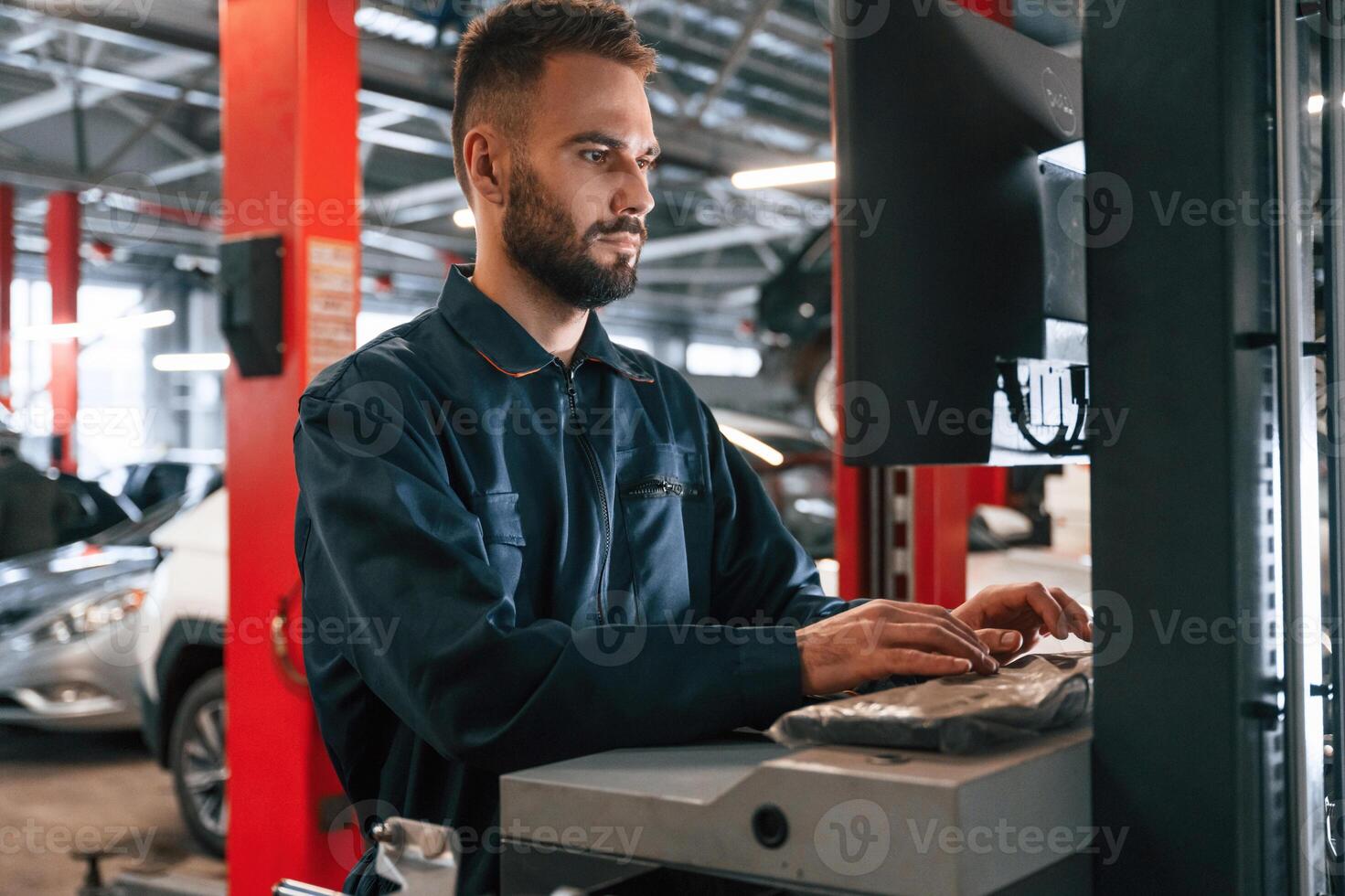 Working by computer.. Car repairman is in the garage with automobile photo