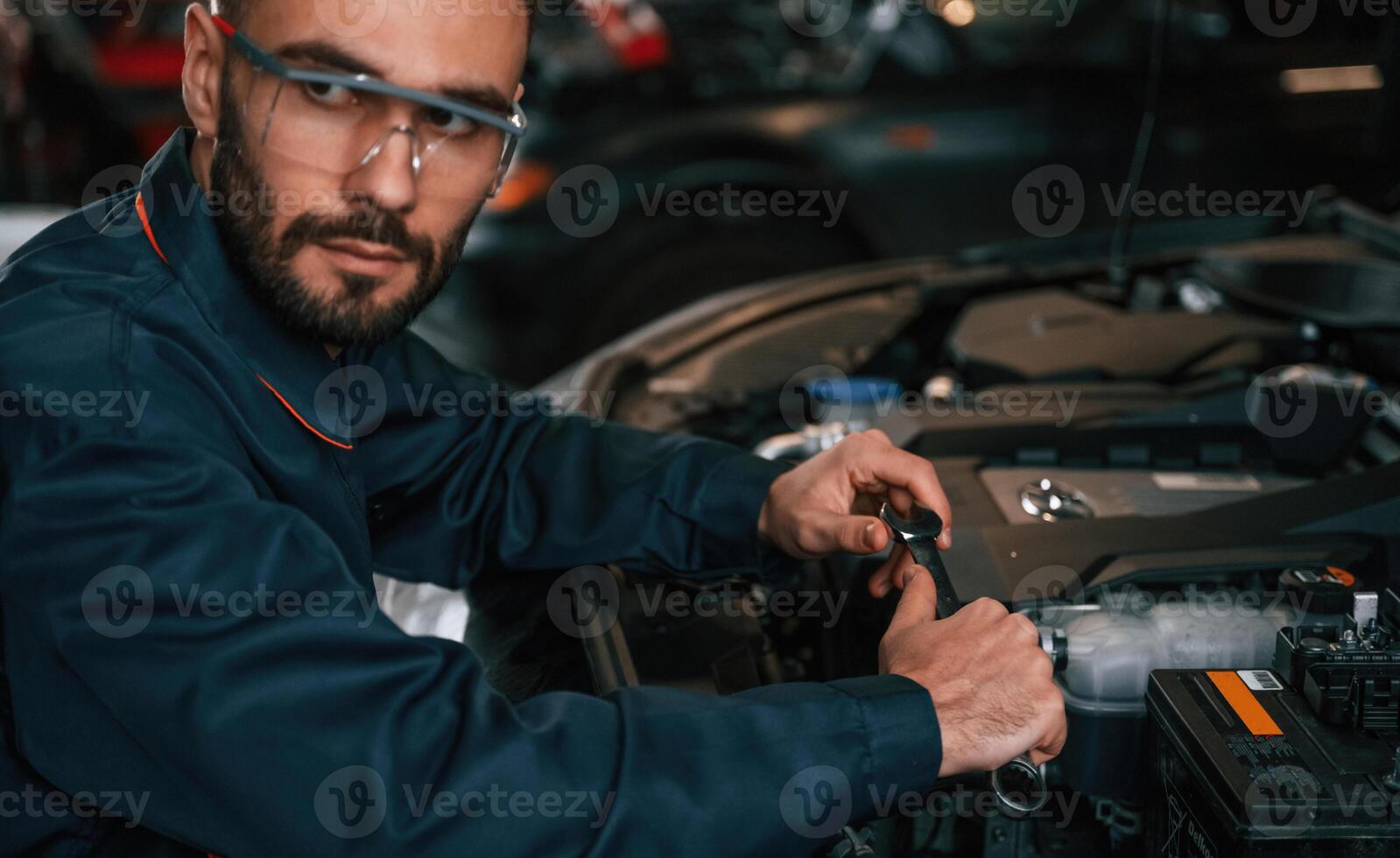 Hood is ,,opened, fixing. Car repairman is in the garage with automobile photo