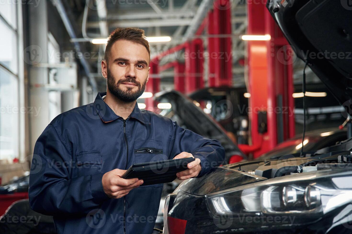 Using ,tablet. Car repairman is in the garage with automobile photo