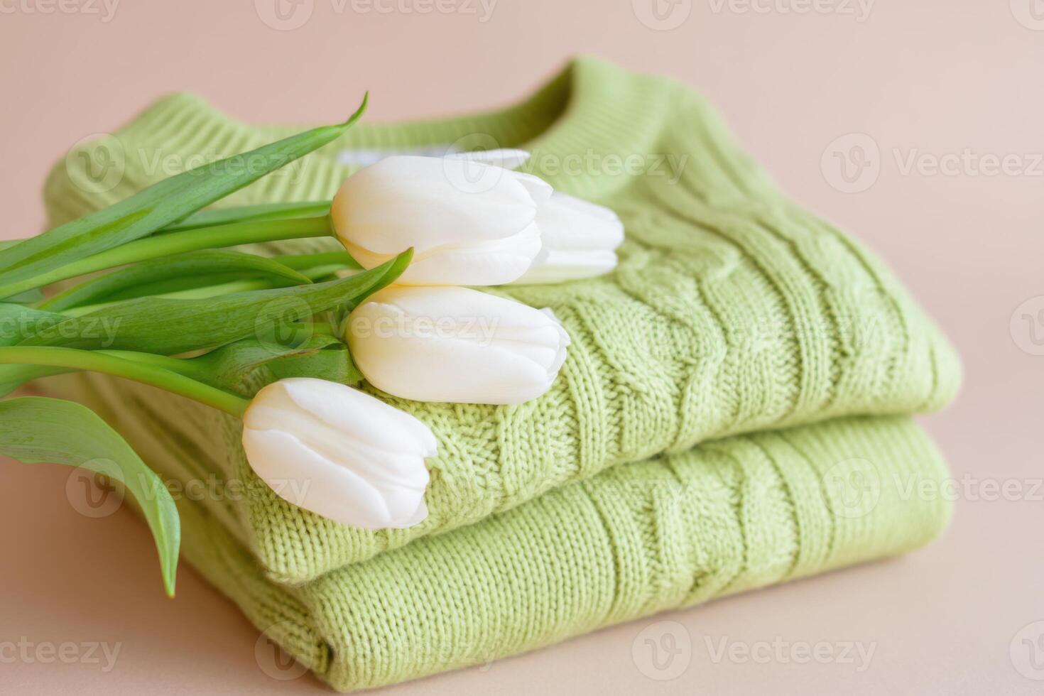 Soft green sweaters stacked with fresh white tulips on a pastel background, showcasing a cozy and inviting atmosphere, spring fashion concept photo