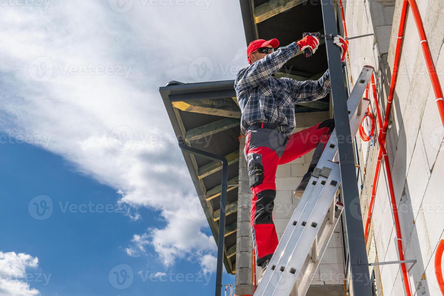 Worker Climbs Ladder to Install Gutter on Construction Site photo