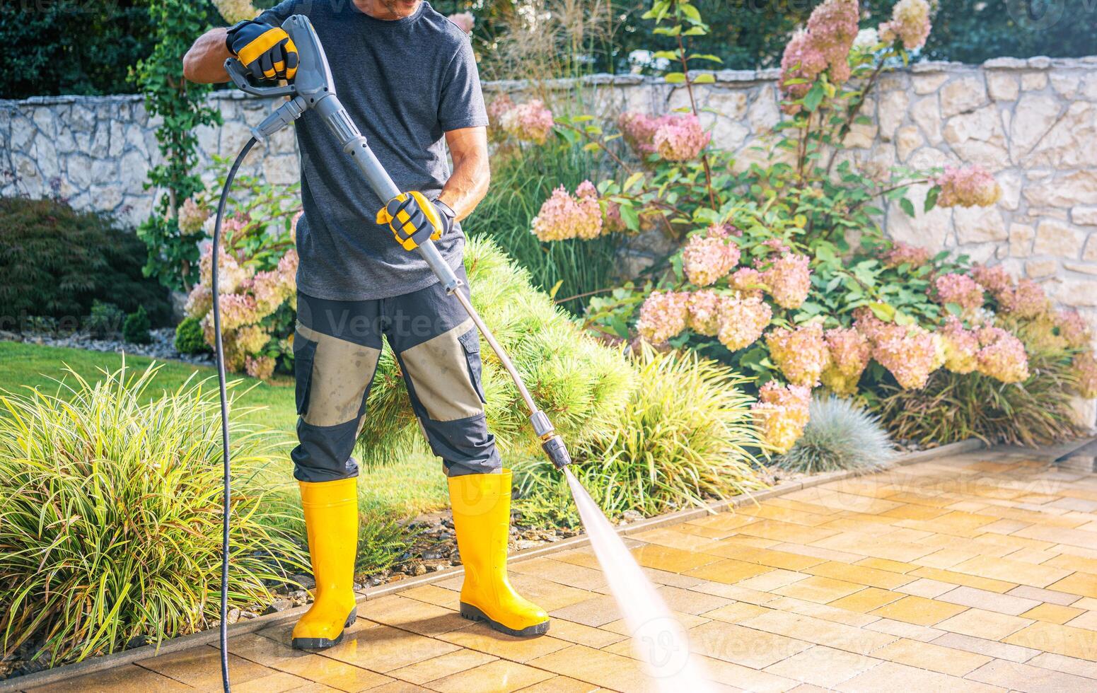 Man Using Pressure Washer to Clean Patio in Garden photo