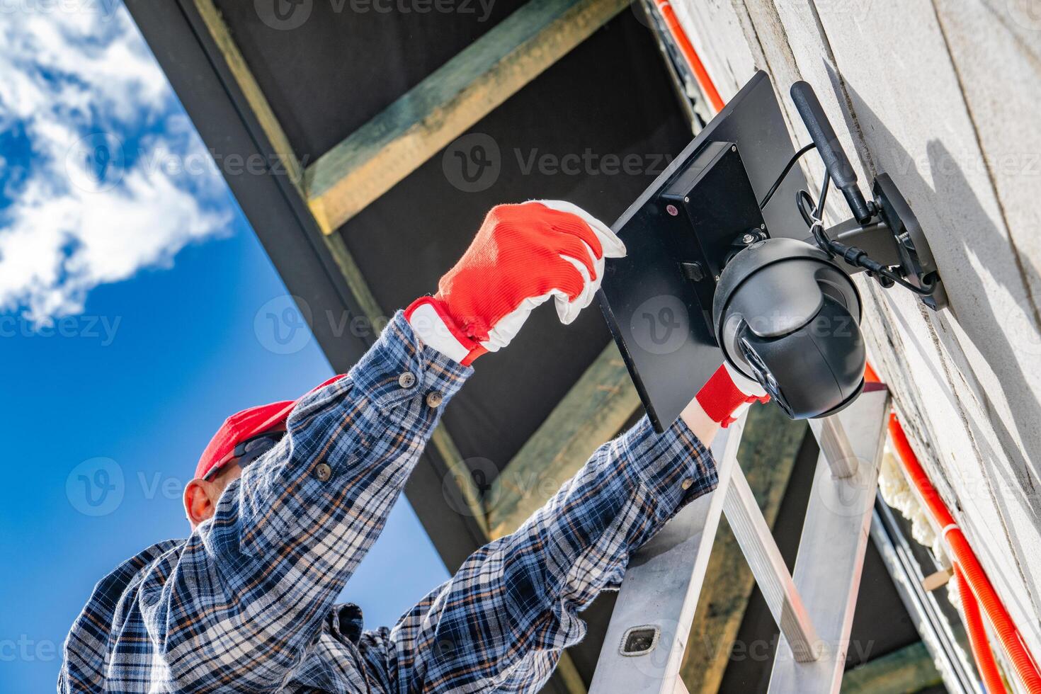 Technician Installs Security Camera on Exterior Wall During Bright Day photo