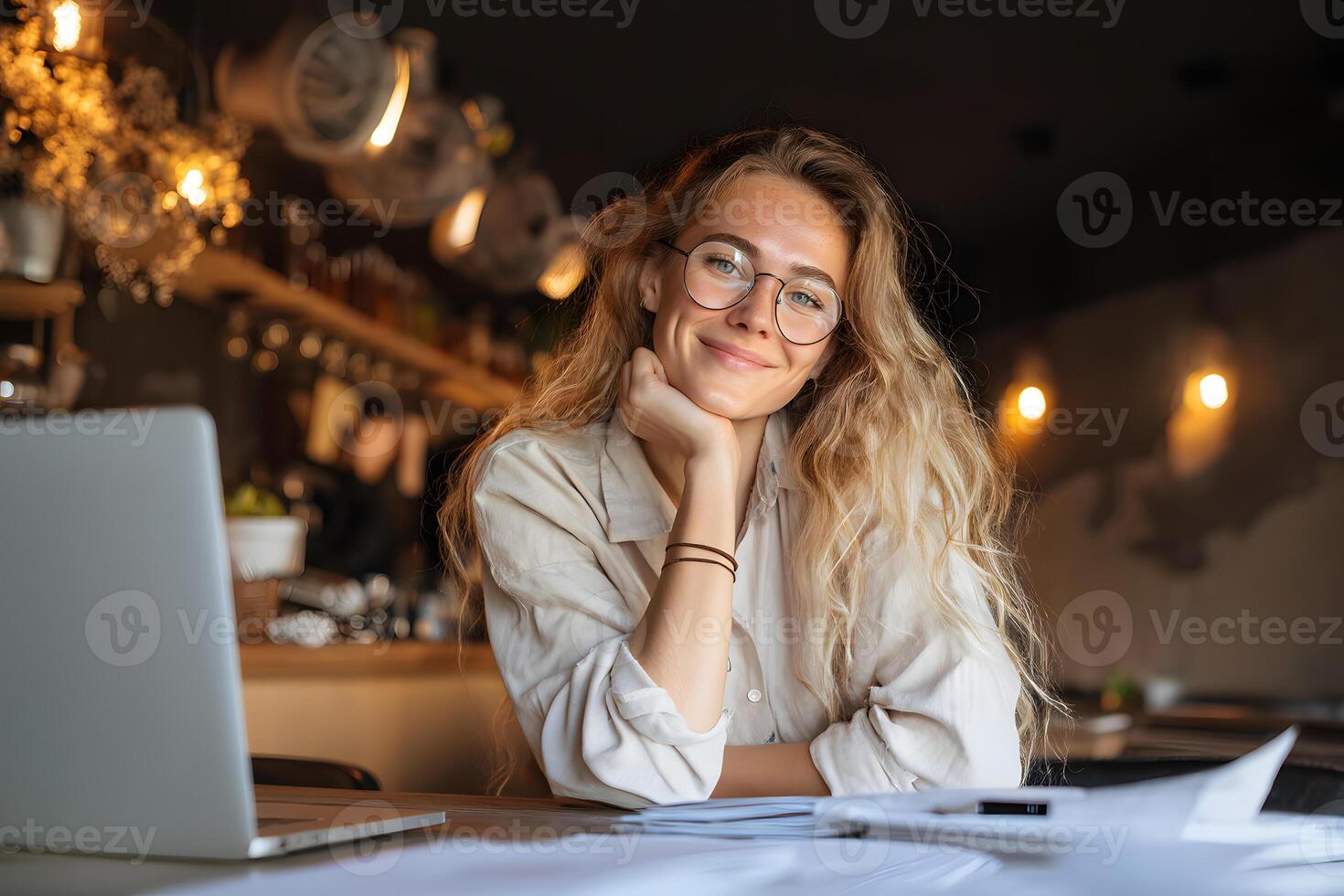 Young woman with stylish glasses sitting at a cozy cafe table, smiling while engaged in her work. photo