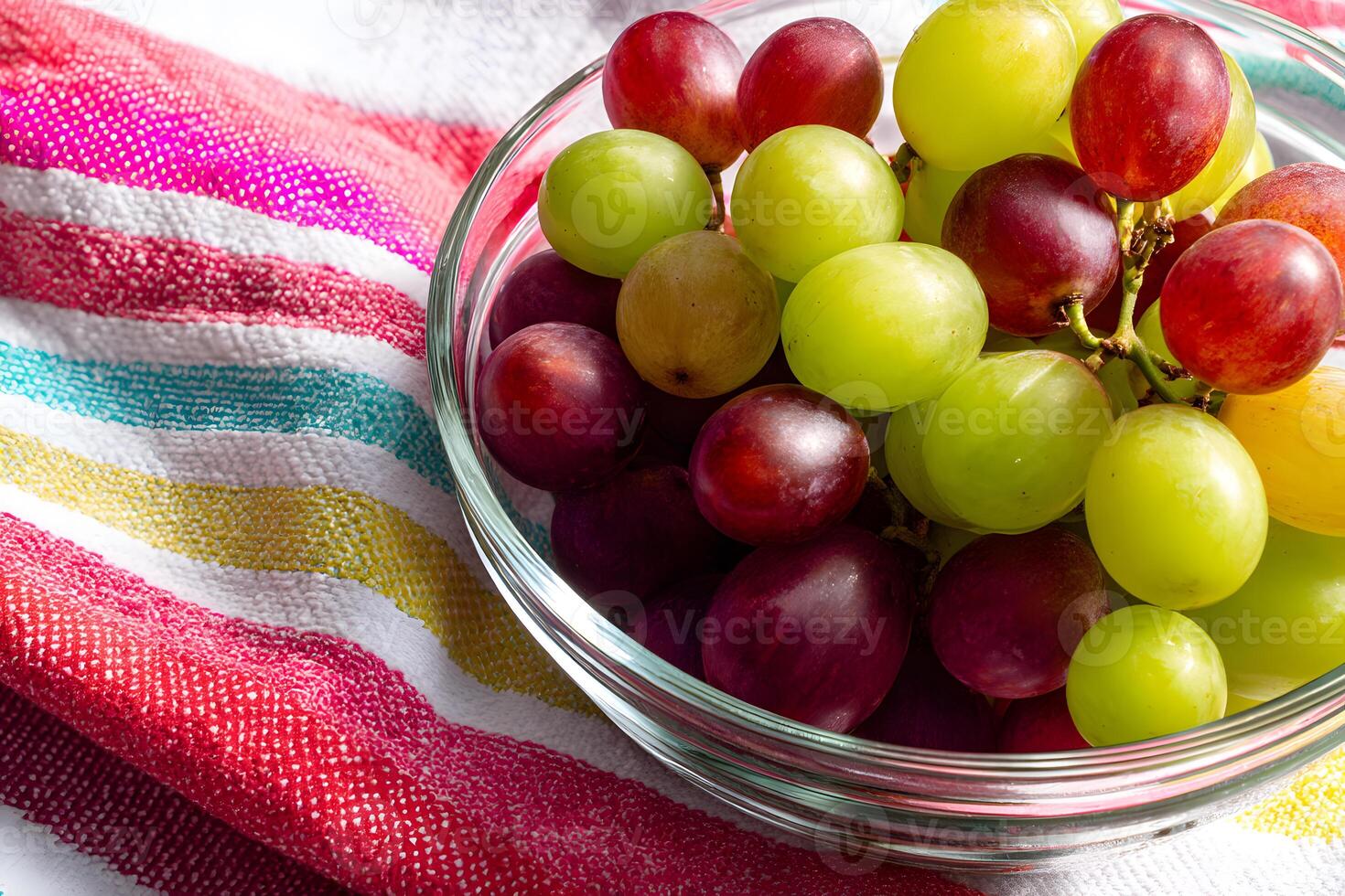 Bowl of green and red grapes set against a vibrant striped beach towel backdrop. photo