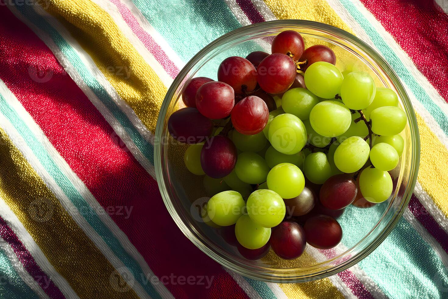 Vibrant glass bowl of fresh green and red grapes on a striped beach towel setting. photo