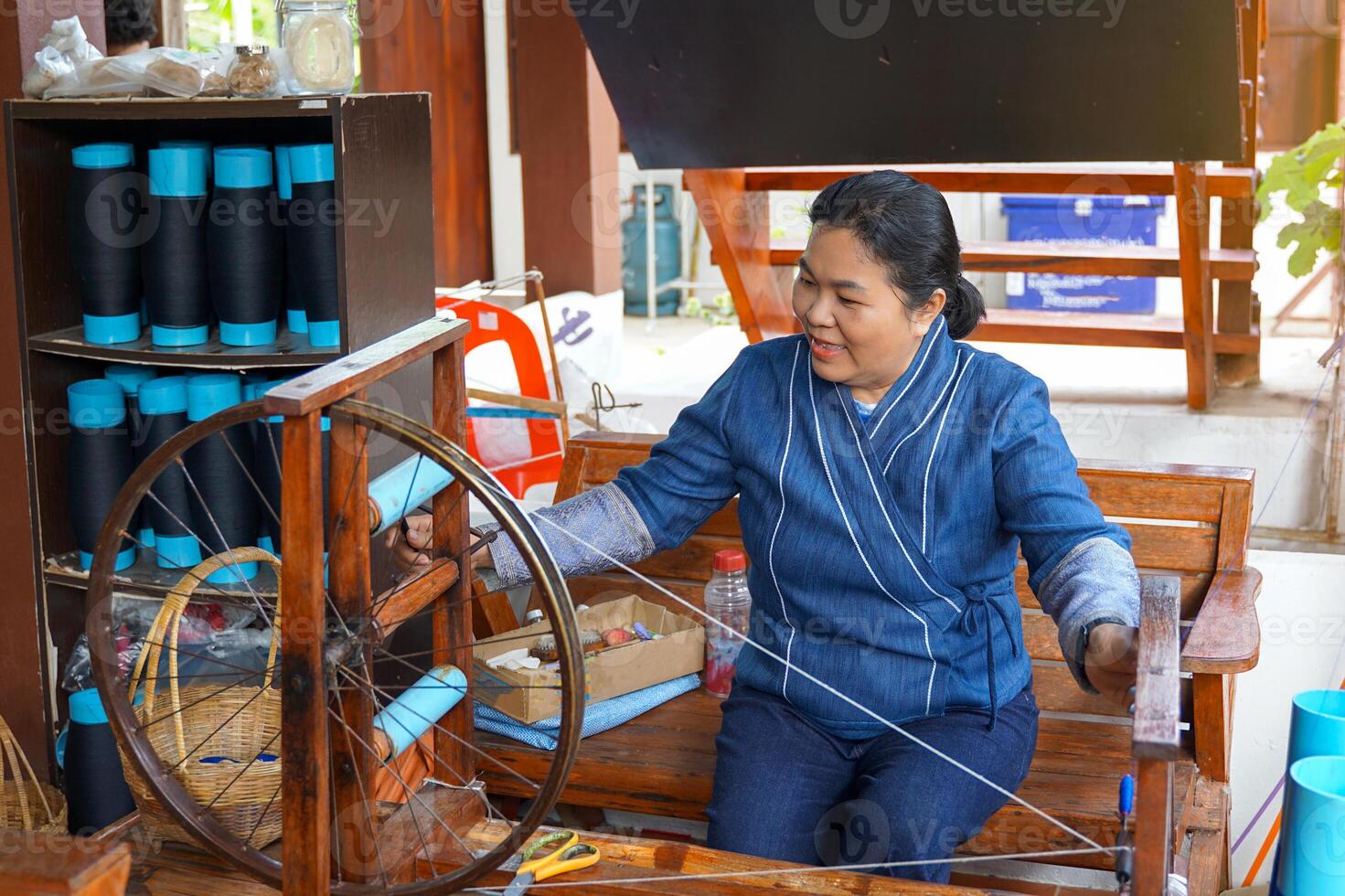 Thai women wearing traditional blue hand-woven clothes use a hand-winding machine. to prepare yarn for weaving in the concept of community products community enterprise Hand weaving photo