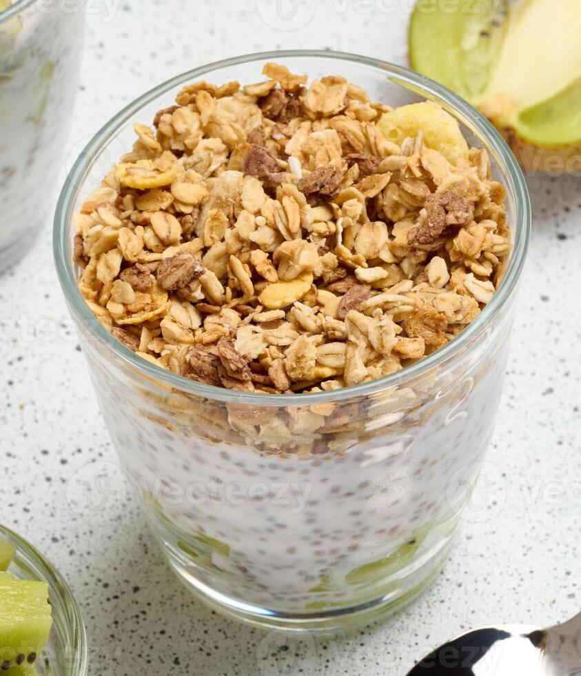 Glass filled with chia seed pudding, layered with diced kiwi at the bottom and topped with crunchy granola. photo