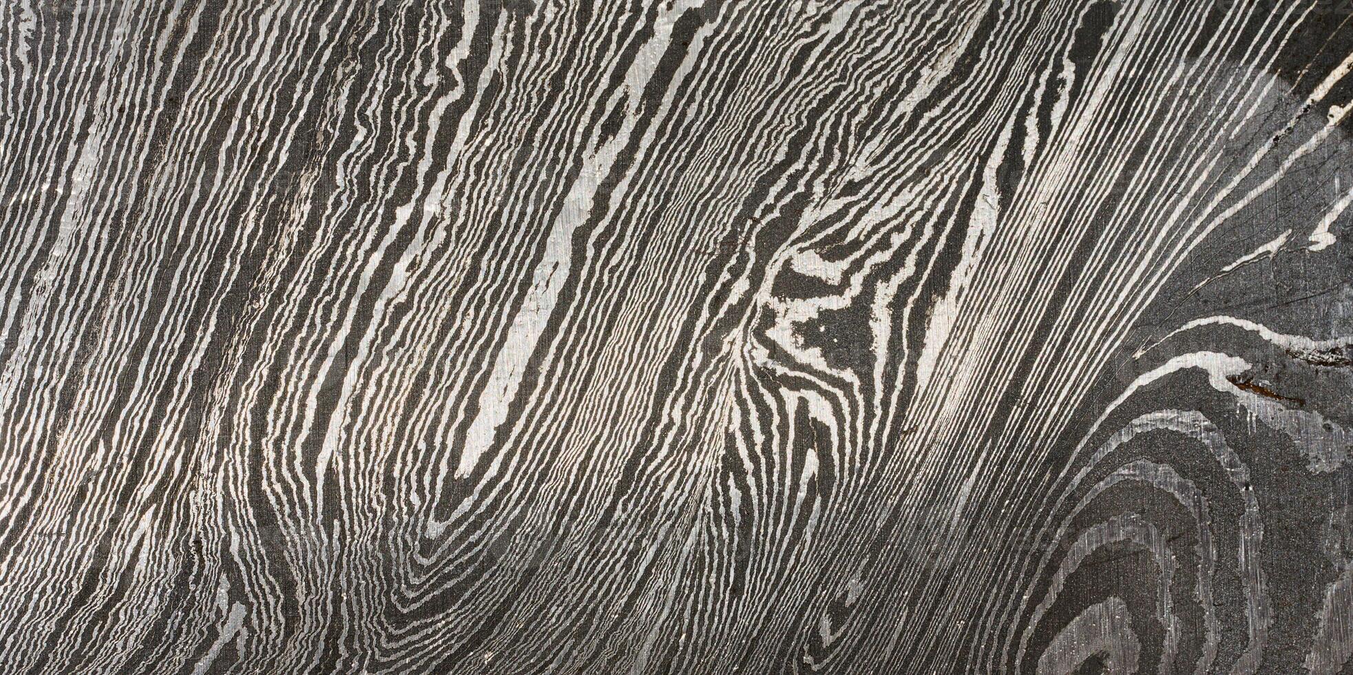 Detailed close up of damascus steel, showcasing its characteristic wavy and layered pattern of light and dark metal. photo