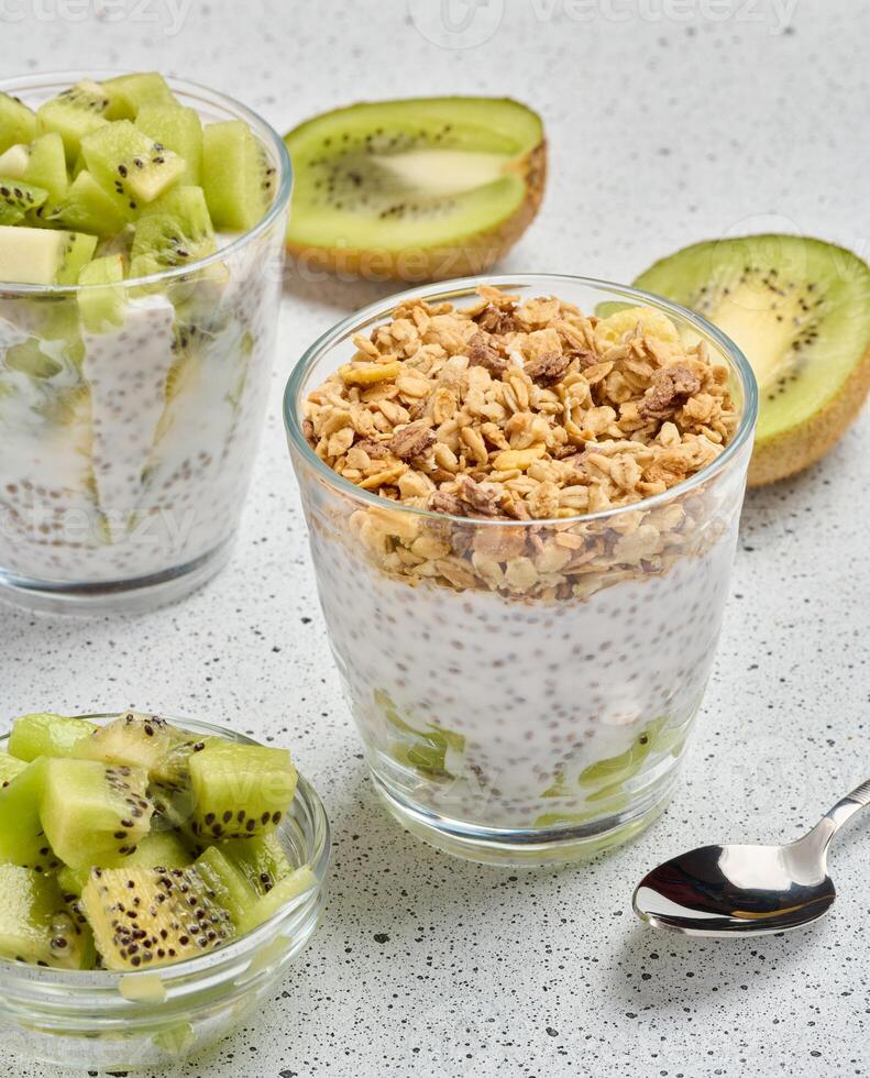 Glass filled with chia seed pudding, layered with diced kiwi at the bottom and topped with crunchy granola photo