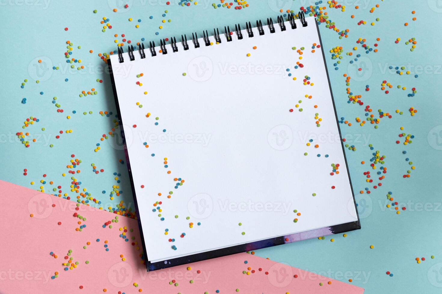 Top view of open notebook with clean sheet on bright vivid blue, pink, background with colorful confetti .Template for message. photo