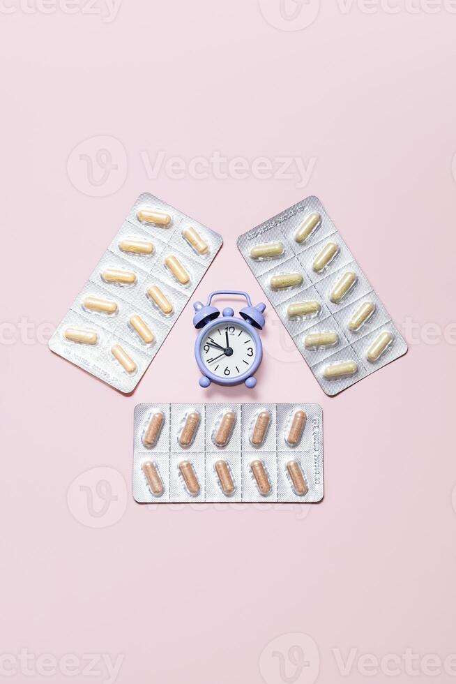 Medicine Blister Packs and Alarm Clock Placed on Pink Background. Importance of Taking Medication on Time to Manage Health and Wellness. photo