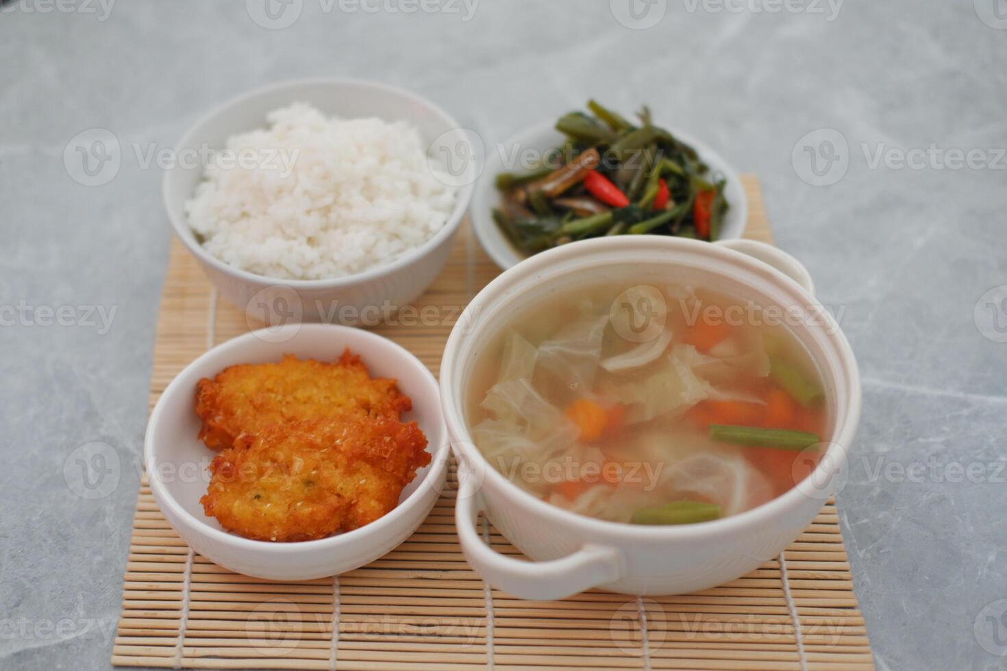 The set includes a bowl of clear vegetable soup filled with cabbage, carrots, and green beans, served in a white bowl with handles photo