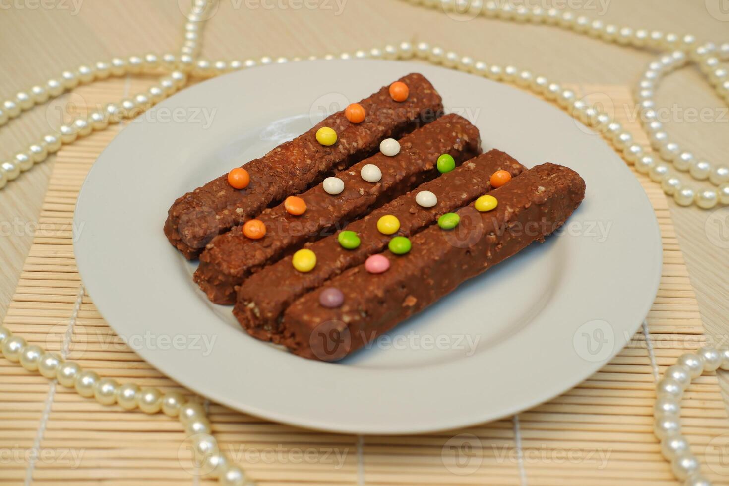 On a smooth, light wooden surface, a white round plate holds several chocolate coated snack bars photo