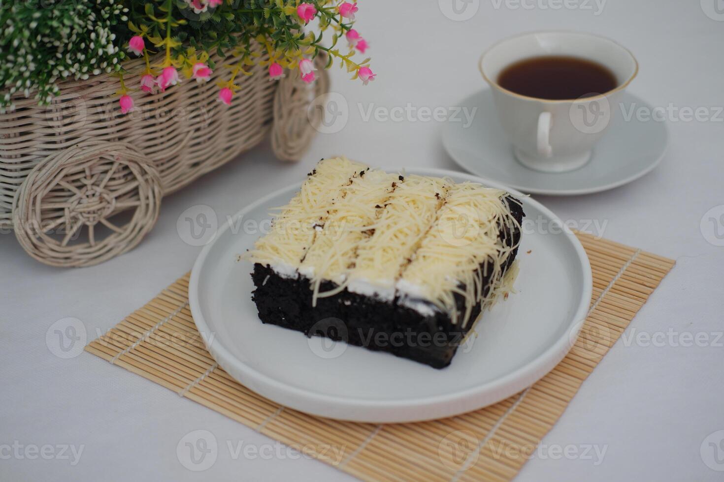 a delicious serving of chocolate sponge cake topped with a generous layer of grated cheese and a thin spread of white cream photo