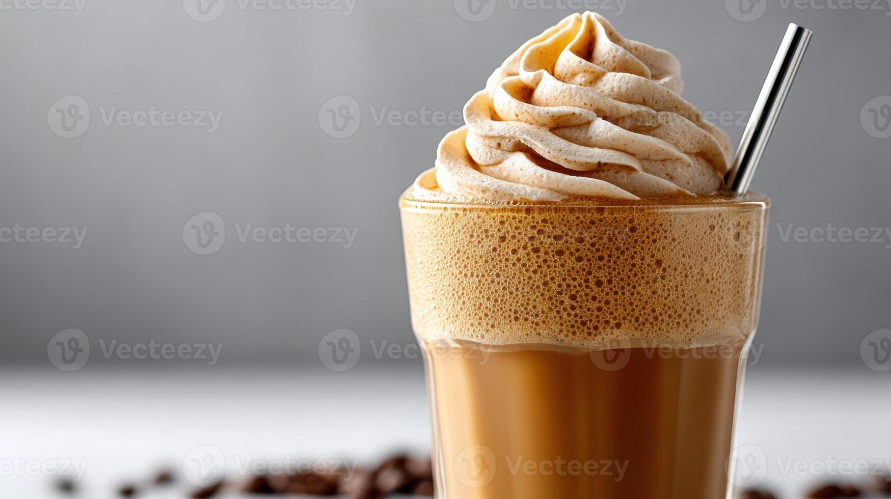 A clear glass cup filled with a creamy iced cappuccino, topped with a generous swirl of frothy milk and a straw inserted at a slight angle photo