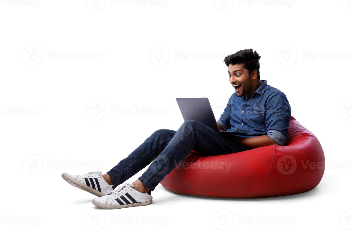 A young male is sitting on a beanbag chair and using his laptop. photo