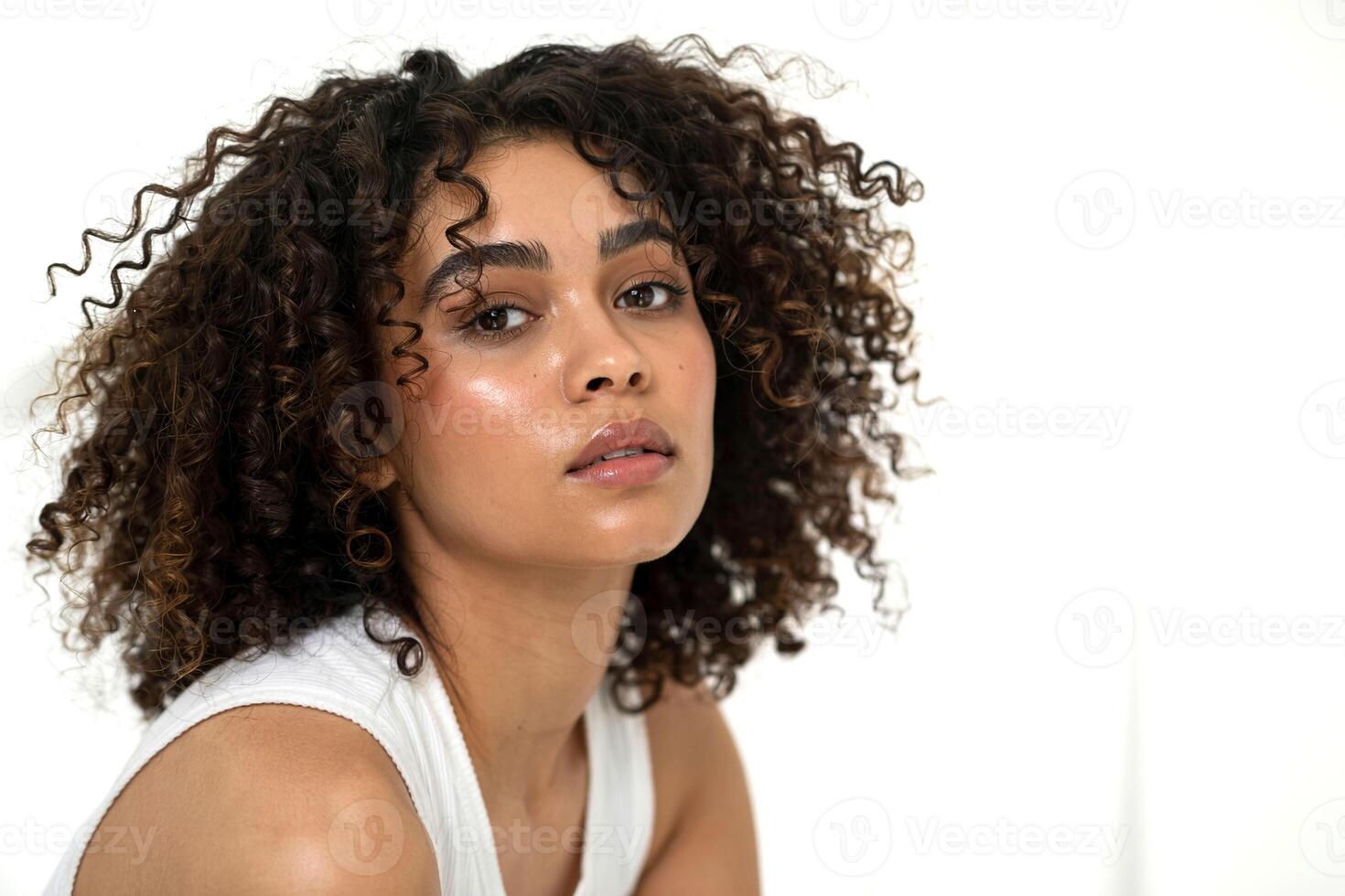A woman with curly hair sitting in front of a white wall photo