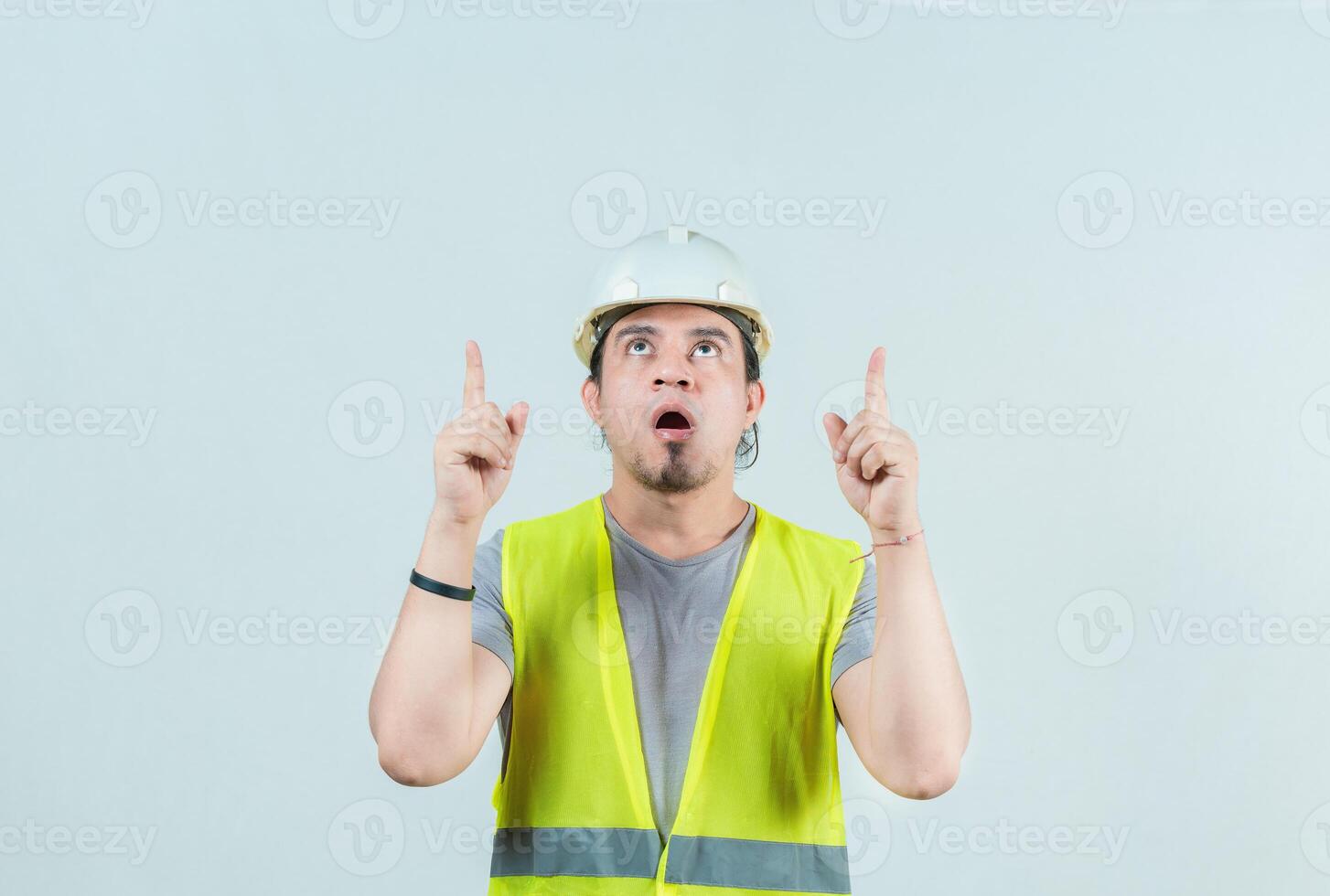 Amazed young builder pointing up, isolated. Surprised construction worker pointing up photo