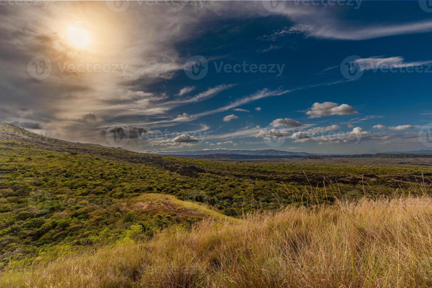 Scenic dry landscape with grassy hills and dramatic cloudy sky at sunset. Hilltop view with cloudy sky and distant mountains at golden hour photo
