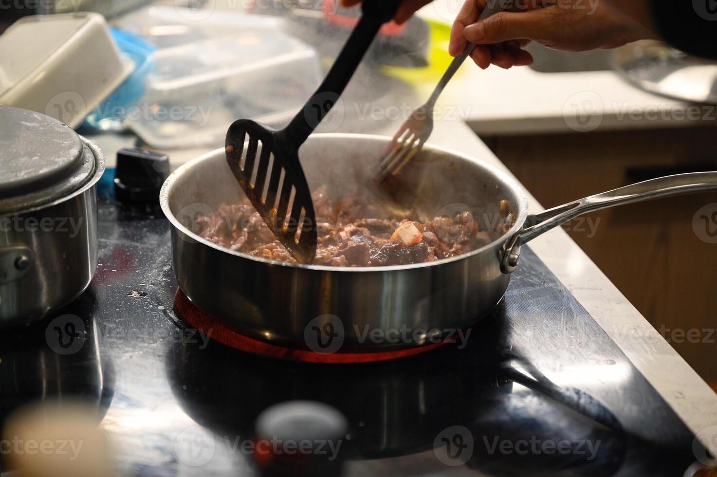 Hand using kitchen flipper frying sliced beef in pan photo