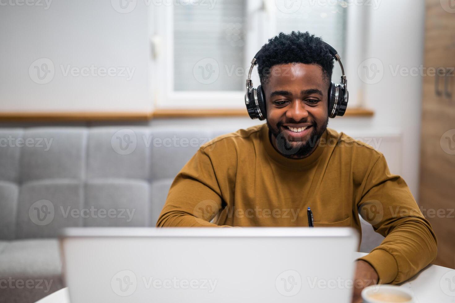A black man watching an online training session and taking notes on his laptop at home. photo