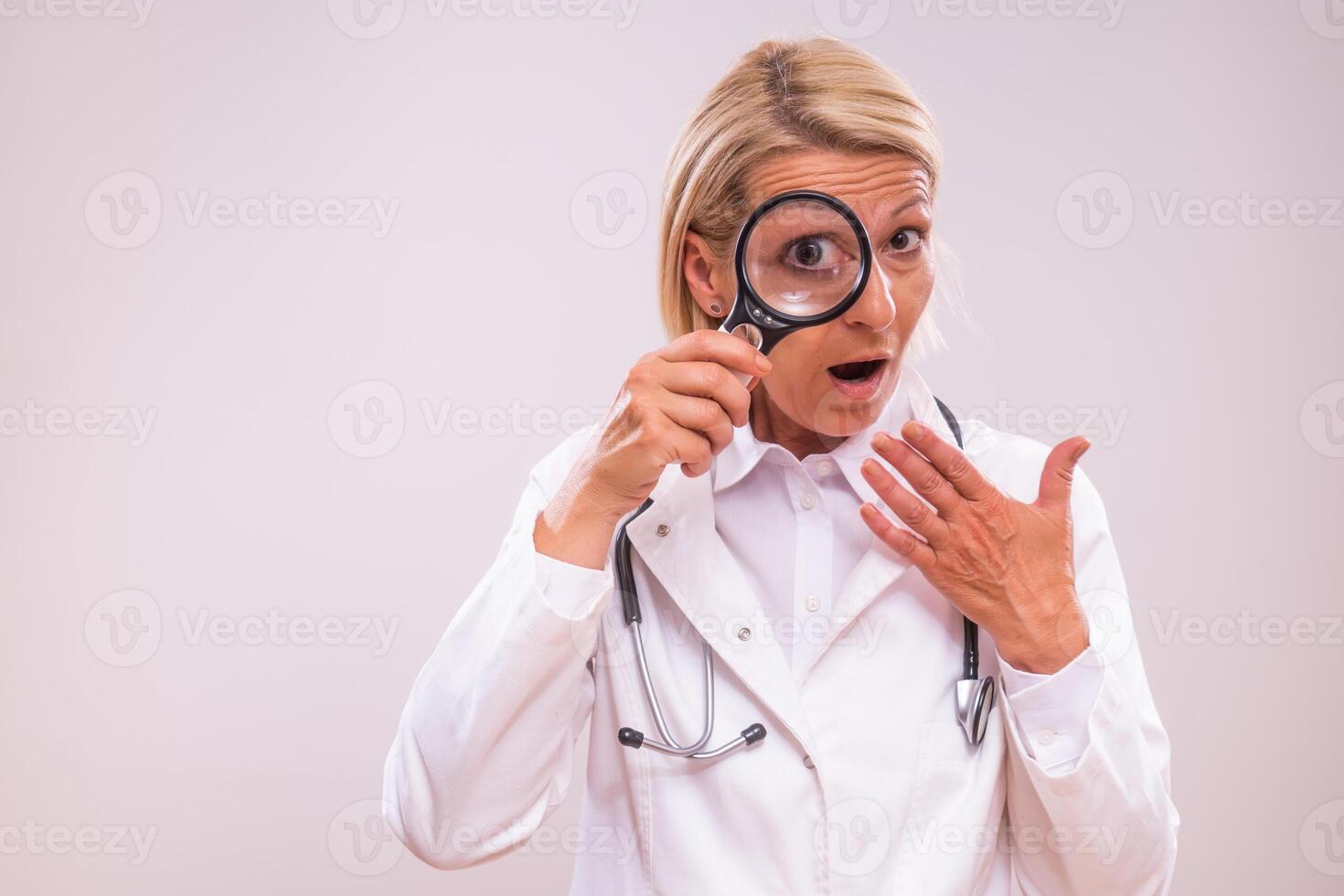 un maduro hembra médico en un blanco laboratorio Saco sostiene un aumentador vaso, curioso en incredulidad como ella examina alguna cosa cercanamente, transporte sorpresa y inquietud. foto