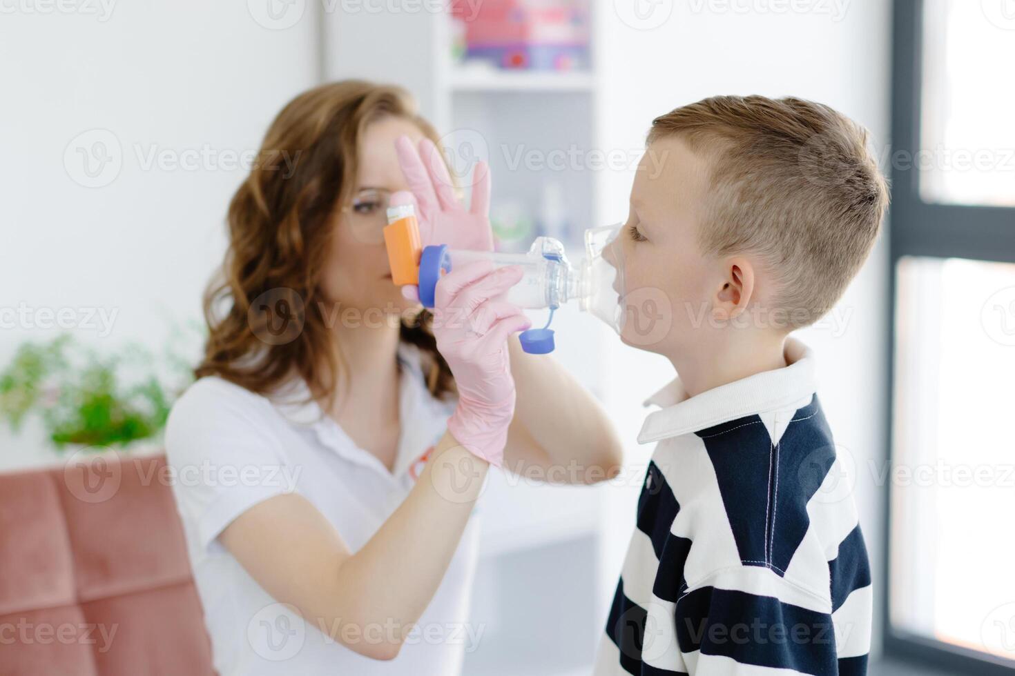 Boy with allergic asthma, inhaling his medication through spacer while sitting in doctors office. photo