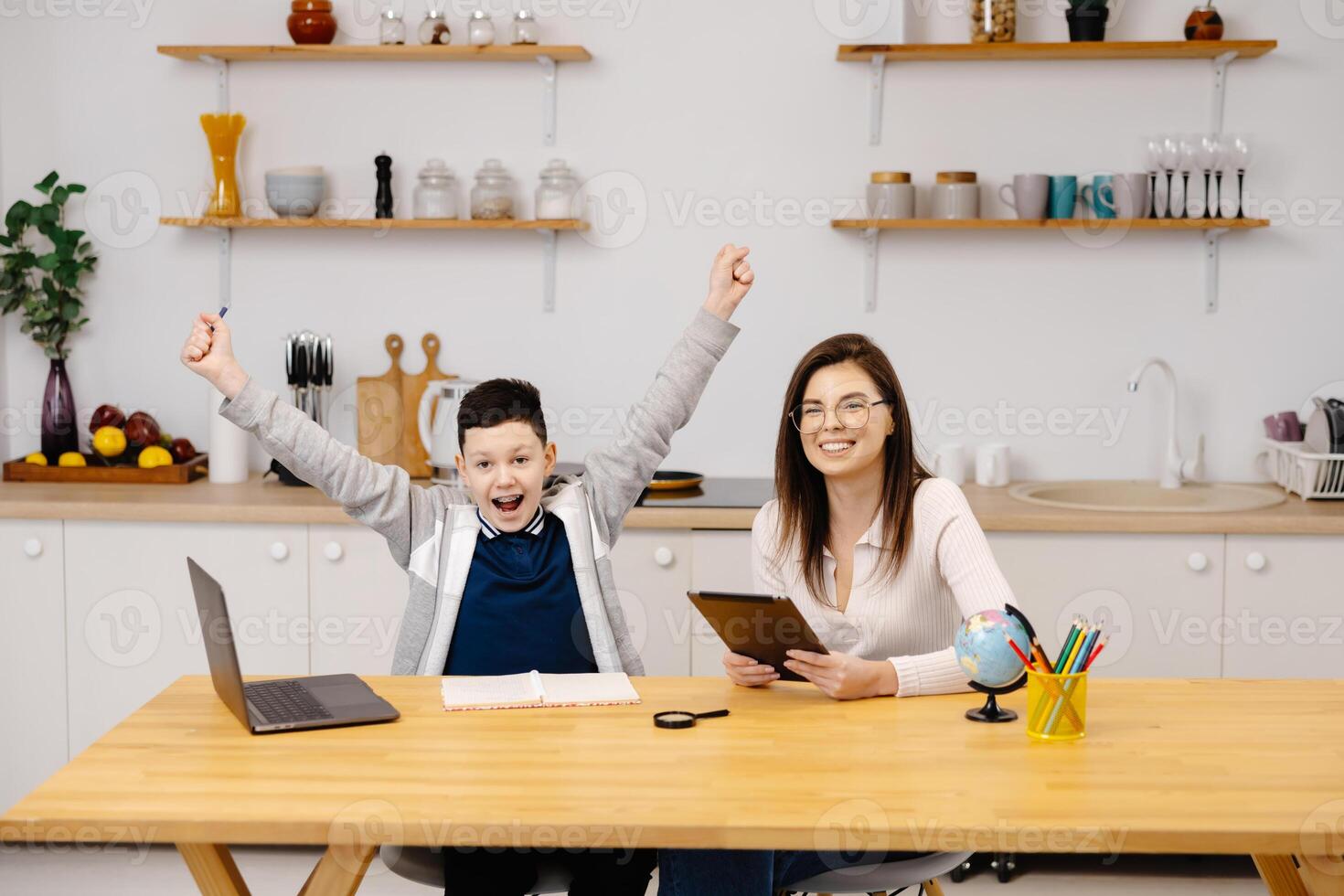 Woman helps a boy with his lessons using a tablet and a globe. A homeschooling student does his homework with the help of a tutor. photo