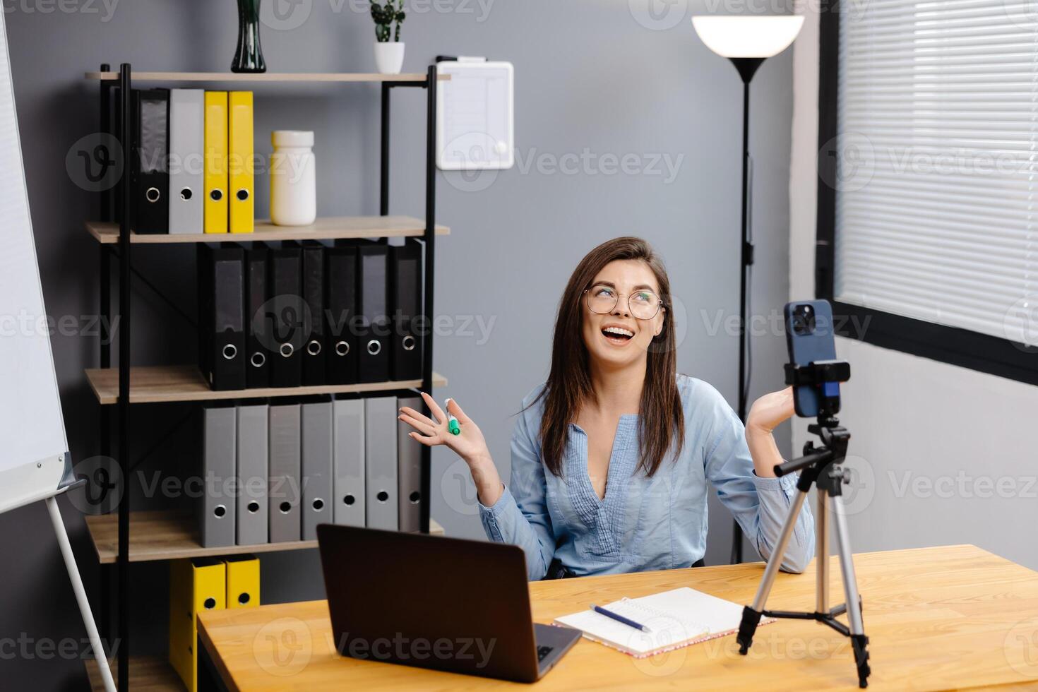 Class of diverse students learning remotely online using web app. Female teacher providing lesson with laptop, recording on cellphone on tripod photo