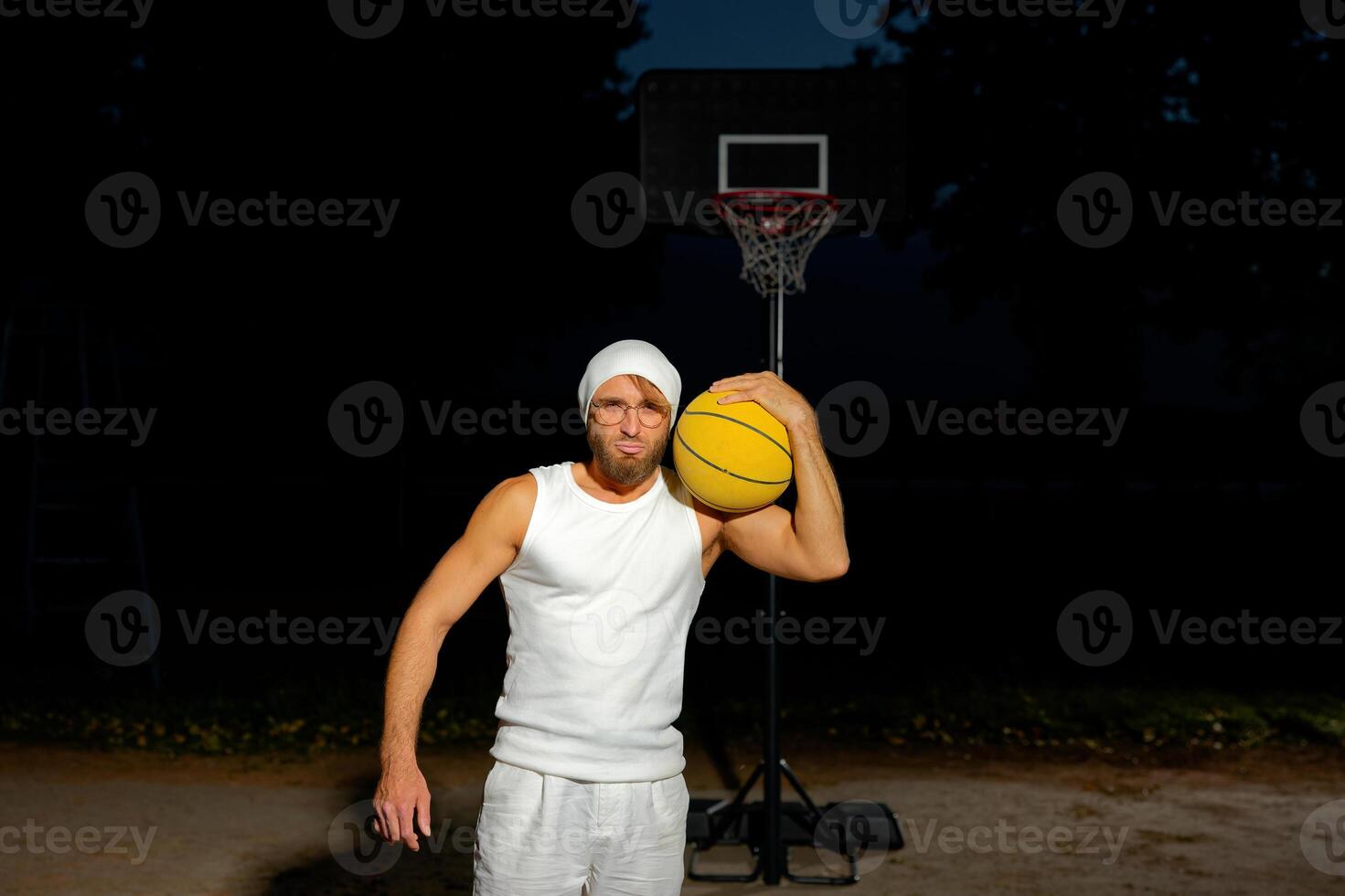 Man holding a basketball in a park at dusk, showcasing athleticism and confidence by the court. photo
