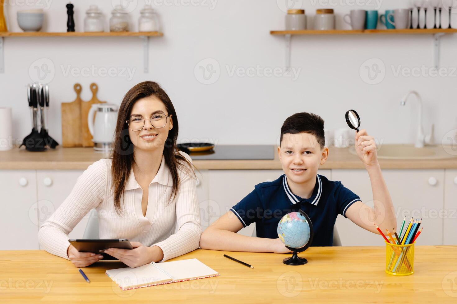 A young woman helps boy with his lessons using a tablet and a globe. A homeschooling student does his homework with the help of a tutor. photo