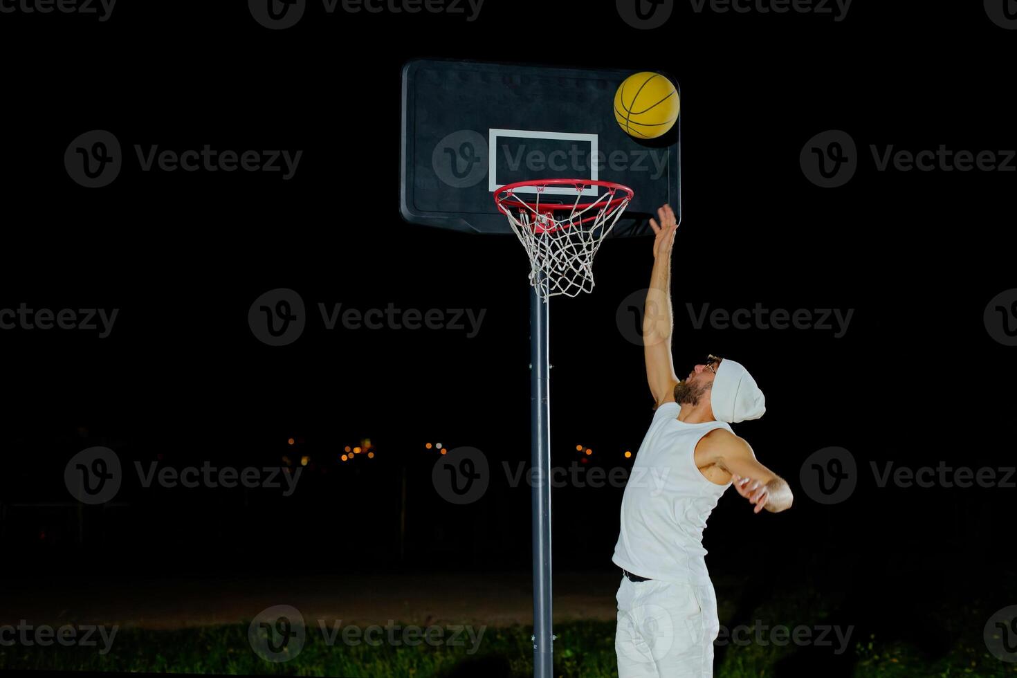 A man performs a slam dunk on a basketball court at night under the glare of bright outdoor lights. photo