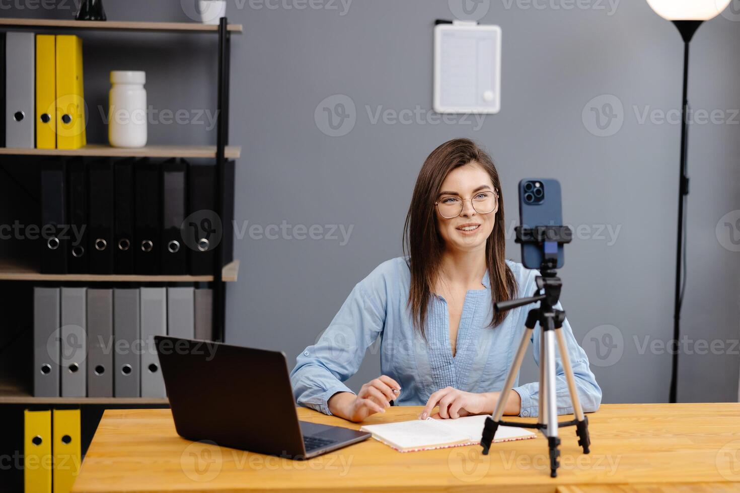 Students learning remotely online using web app. Female teacher providing lesson with laptop, recording on cellphone on tripod photo