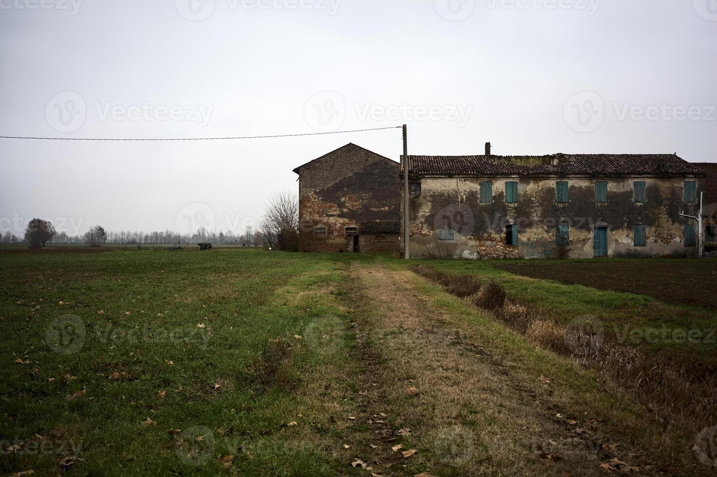 Abandoned farmhouse and a path in a field on a cloudy day in the italian countryside photo