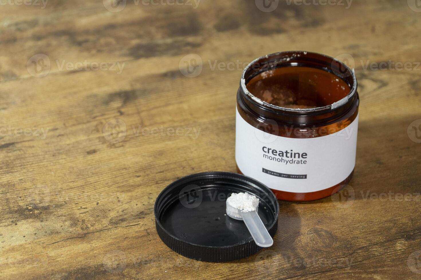 Creatine monohydrate powder in the measuring spoon and jar on wooden table photo
