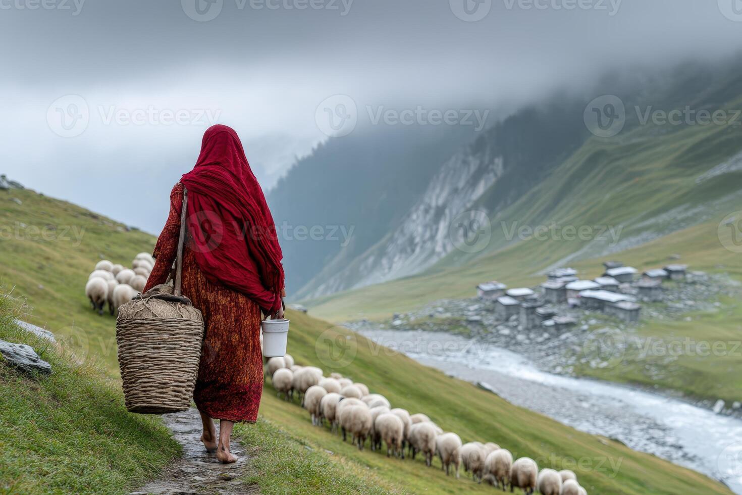 Woman herding sheep through a lush green valley in the mountains during a cloudy day photo