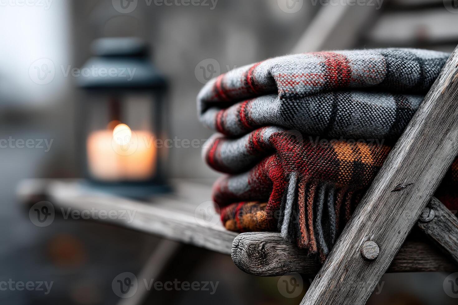Cozy blankets stacked on a wooden chair beside a glowing lantern in a tranquil outdoor setting during early evening photo