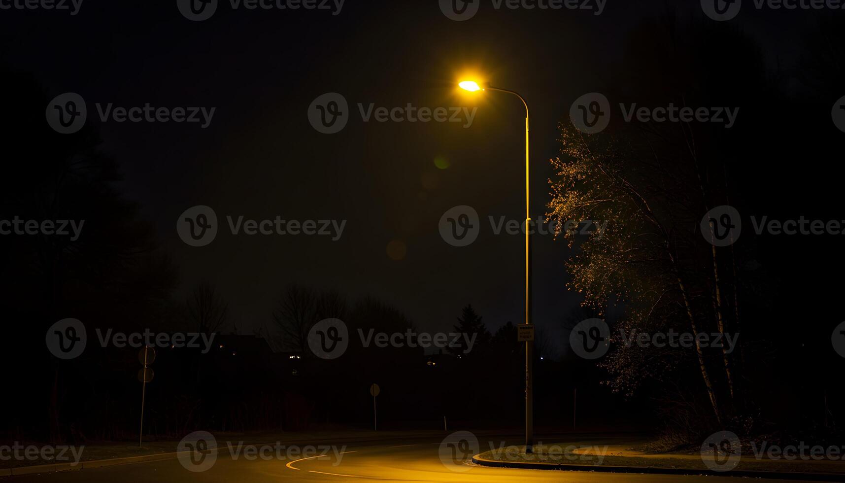 Nighttime road illuminated by warm streetlights with wet pavement trees and guardrail in serene night scene photo