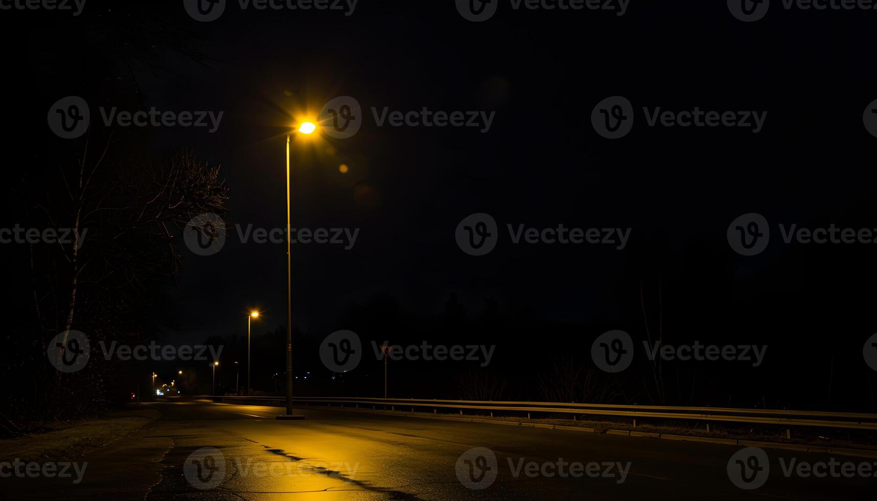 Nighttime road with wet pavement illuminated by warm yellow streetlights surrounded by trees photo