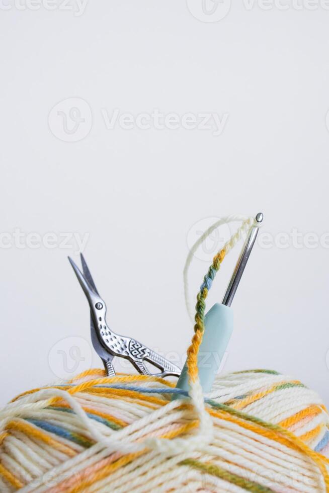 Multicolored yarn ball with crochet hook and scissors on white background photo
